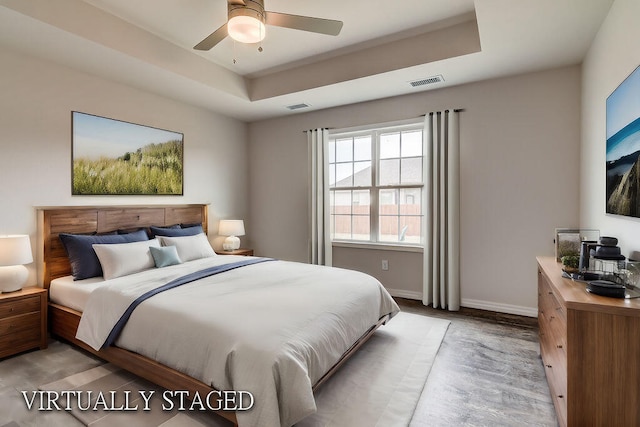 bedroom featuring ceiling fan, light hardwood / wood-style floors, and a tray ceiling