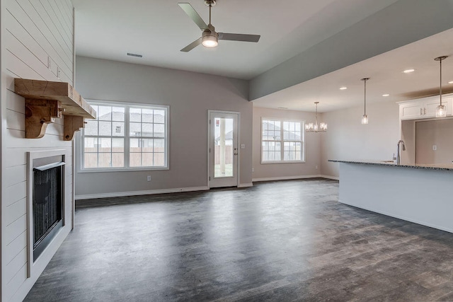 unfurnished living room with sink, plenty of natural light, and ceiling fan with notable chandelier