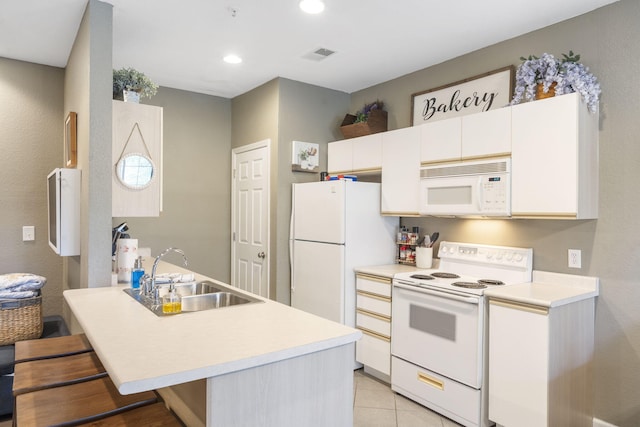 kitchen with white cabinets, light tile patterned floors, a kitchen bar, sink, and white appliances