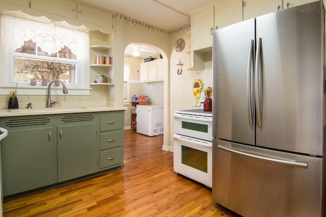 kitchen featuring sink, green cabinetry, stainless steel fridge, light hardwood / wood-style floors, and white range oven