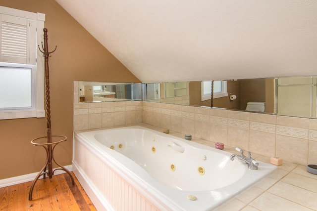 bathroom featuring lofted ceiling, wood-type flooring, toilet, and tiled tub