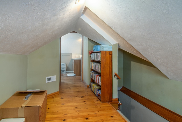 bonus room featuring light hardwood / wood-style floors, lofted ceiling, and a textured ceiling