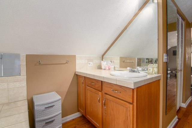 bathroom with a textured ceiling, hardwood / wood-style floors, tile walls, vaulted ceiling, and vanity