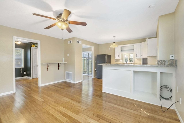 kitchen featuring plenty of natural light, kitchen peninsula, black fridge, and white cabinets