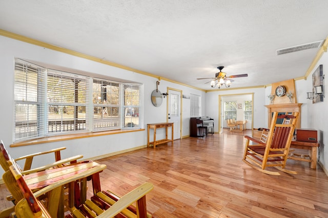 living area featuring crown molding, a textured ceiling, light hardwood / wood-style flooring, and ceiling fan