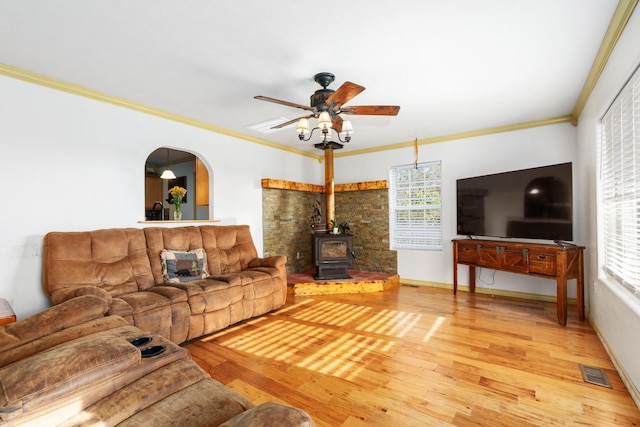 living room with a wood stove, ceiling fan, wood-type flooring, and crown molding