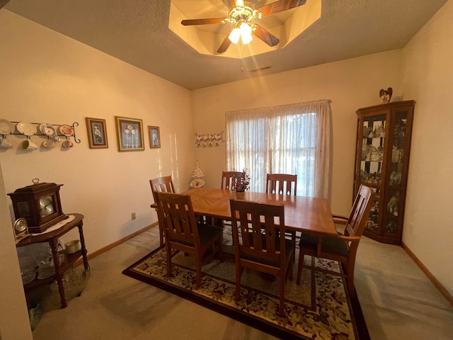 carpeted dining area with a textured ceiling, a tray ceiling, and ceiling fan