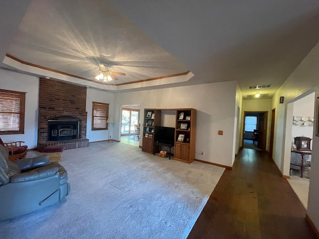 living room with a wood stove, wood-type flooring, a raised ceiling, and ceiling fan