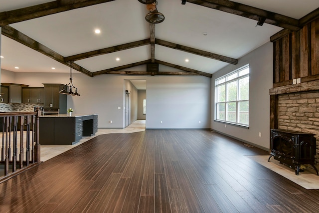 unfurnished living room featuring vaulted ceiling with beams, light hardwood / wood-style flooring, and a wood stove