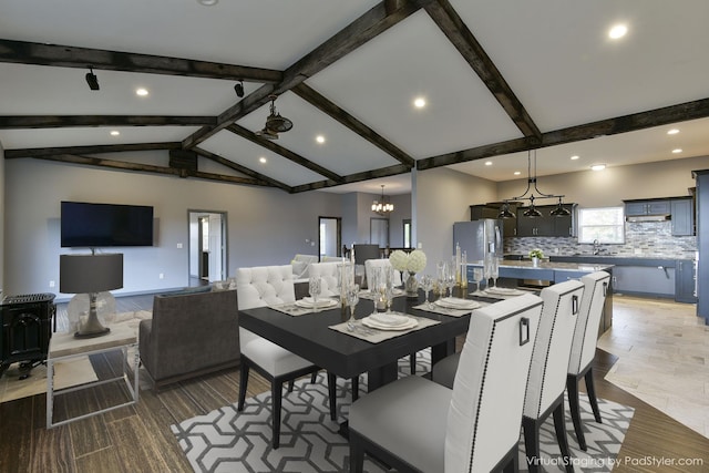 dining space featuring wood-type flooring, a chandelier, and vaulted ceiling with beams