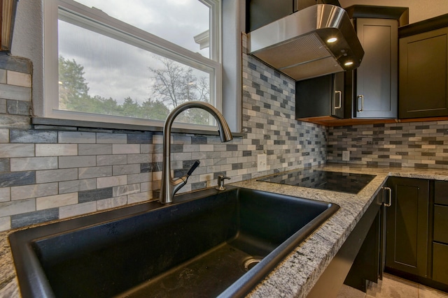 details featuring black electric stovetop, wall chimney range hood, backsplash, sink, and light stone counters