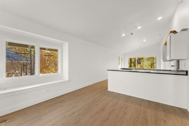 interior space featuring a healthy amount of sunlight, white cabinetry, light hardwood / wood-style floors, and lofted ceiling