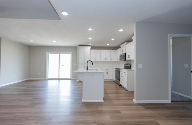 kitchen with a center island with sink, white cabinetry, light wood-type flooring, sink, and stainless steel appliances