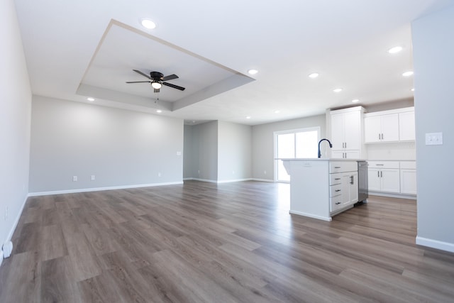 unfurnished living room featuring light hardwood / wood-style floors, a raised ceiling, sink, and ceiling fan