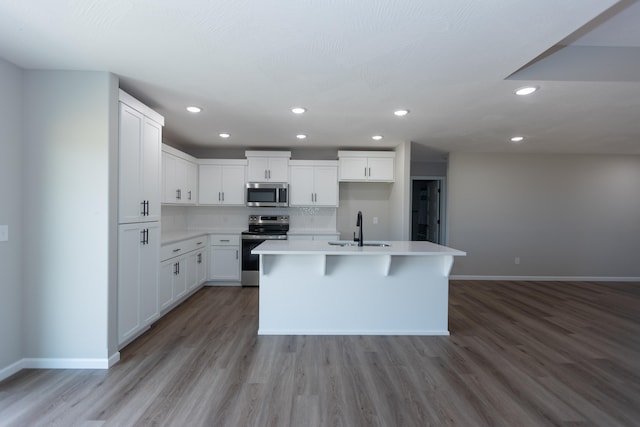 kitchen with stainless steel appliances, a center island with sink, sink, white cabinetry, and light hardwood / wood-style floors