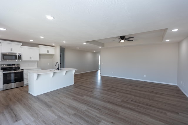 kitchen with appliances with stainless steel finishes, a kitchen island with sink, white cabinets, and hardwood / wood-style flooring