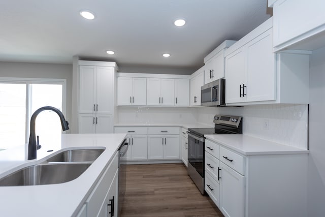 kitchen featuring dark wood-type flooring, stainless steel appliances, sink, white cabinets, and tasteful backsplash