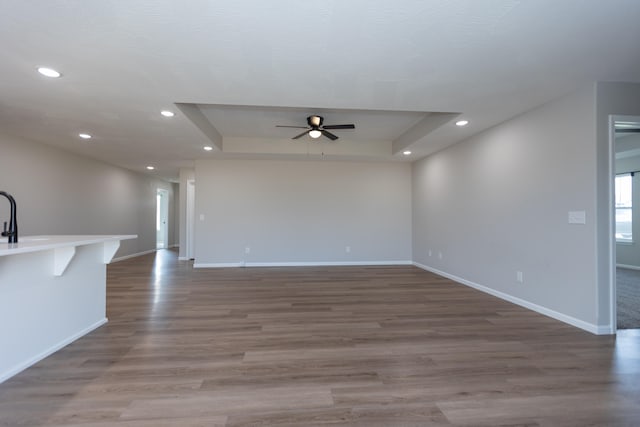 unfurnished living room featuring sink, ceiling fan, a tray ceiling, and dark hardwood / wood-style flooring