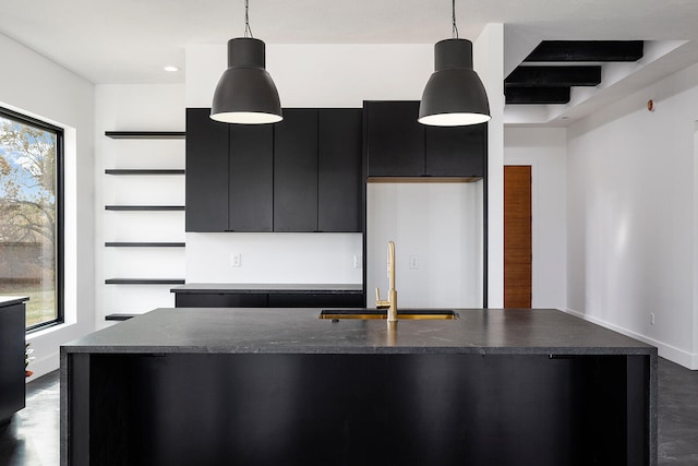 kitchen featuring sink, beamed ceiling, decorative light fixtures, and an island with sink