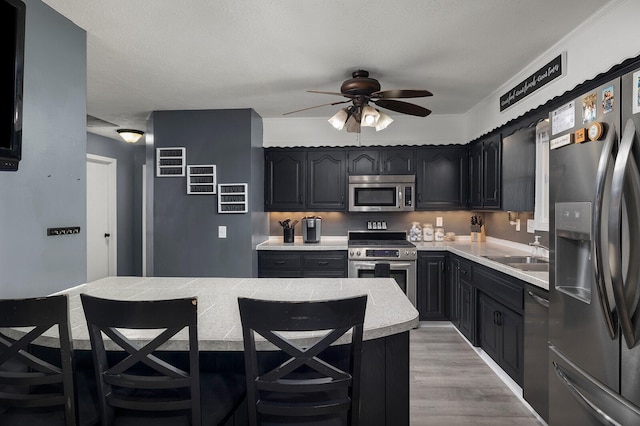 kitchen featuring a kitchen breakfast bar, a textured ceiling, light wood-type flooring, sink, and stainless steel appliances