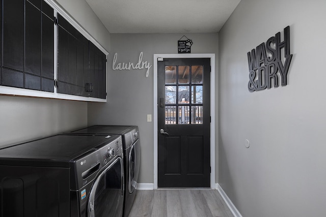 laundry area featuring a textured ceiling, washing machine and dryer, light hardwood / wood-style floors, and cabinets