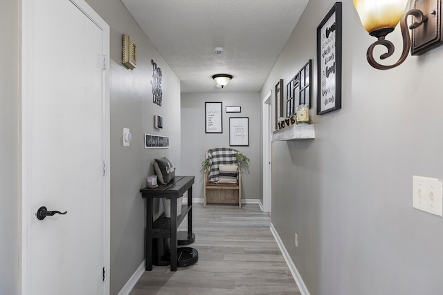 hall with a textured ceiling and light wood-type flooring