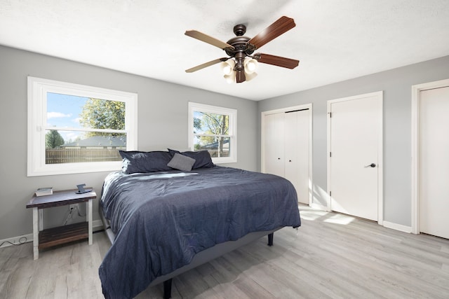 bedroom with ceiling fan, multiple closets, and light hardwood / wood-style floors