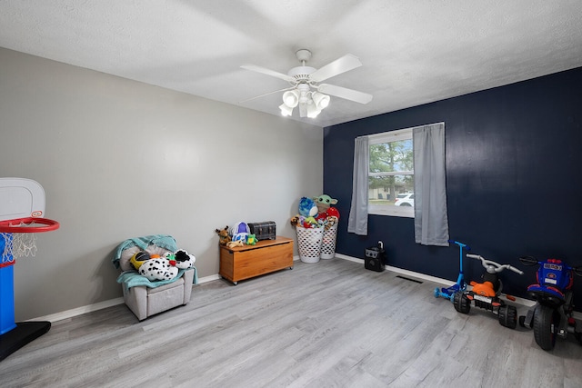 game room with ceiling fan, a textured ceiling, and light wood-type flooring