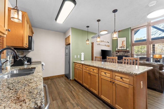 kitchen featuring sink, stainless steel fridge, pendant lighting, light stone counters, and dark hardwood / wood-style floors