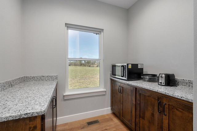 kitchen featuring light hardwood / wood-style floors, dark brown cabinetry, and light stone countertops