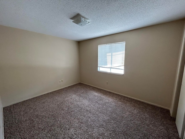 spare room featuring a textured ceiling and dark colored carpet