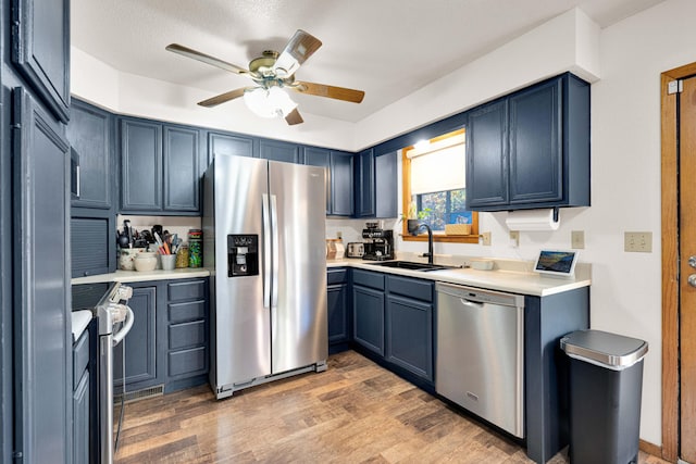 kitchen with wood-type flooring, blue cabinetry, appliances with stainless steel finishes, and sink