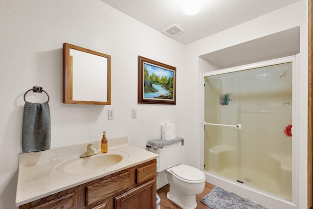 bathroom featuring hardwood / wood-style flooring, toilet, vanity, a textured ceiling, and an enclosed shower