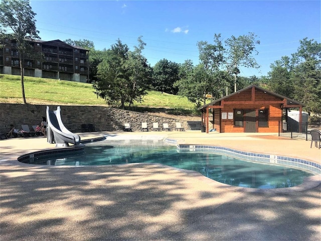 view of swimming pool with a patio area, a water slide, and a lawn