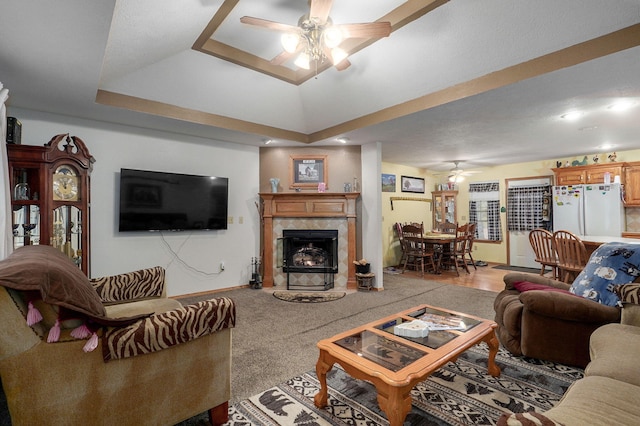 living room with a premium fireplace, light carpet, a tray ceiling, and ceiling fan