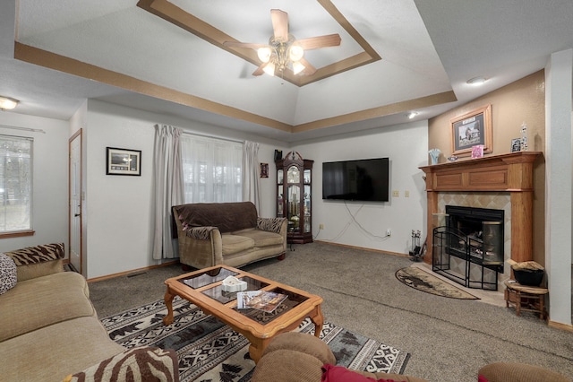 living room featuring ceiling fan, carpet flooring, a tile fireplace, and a raised ceiling