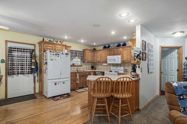 kitchen with decorative backsplash, a breakfast bar area, kitchen peninsula, light wood-type flooring, and white appliances