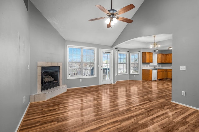 unfurnished living room with a tile fireplace, dark hardwood / wood-style floors, high vaulted ceiling, and ceiling fan