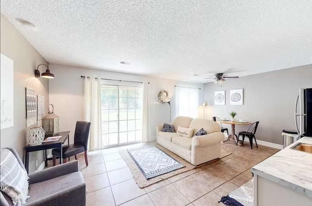 living room with ceiling fan, a textured ceiling, and light tile patterned floors