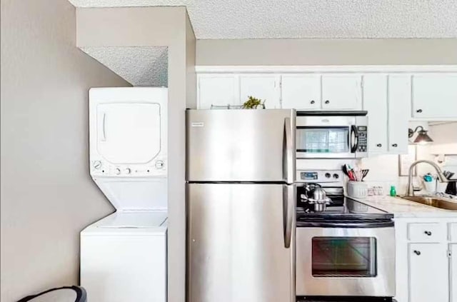 kitchen with white cabinets, a textured ceiling, sink, stainless steel appliances, and stacked washer and clothes dryer