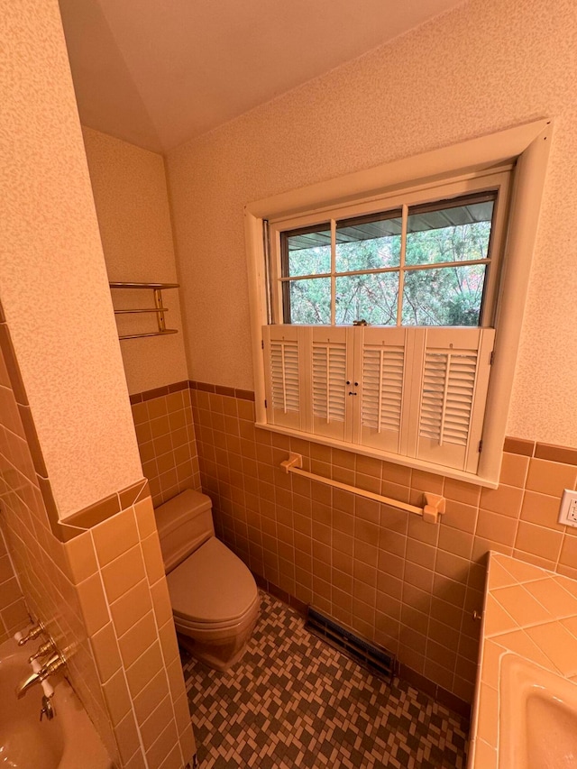 bathroom featuring a bath, toilet, and tile walls