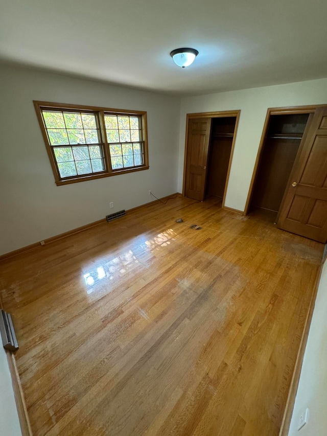 unfurnished bedroom with light hardwood / wood-style floors and two closets