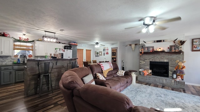 living room featuring dark wood-type flooring, sink, a brick fireplace, a textured ceiling, and ceiling fan