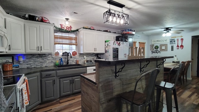 kitchen featuring white appliances, sink, white cabinetry, gray cabinets, and a breakfast bar