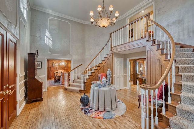 foyer with a towering ceiling, a chandelier, light wood-type flooring, and ornamental molding