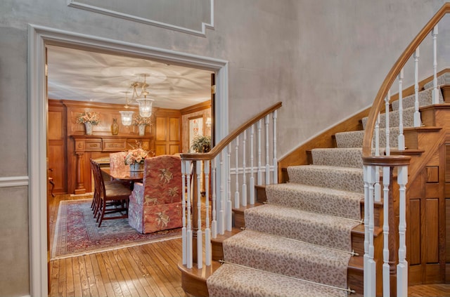 stairway with a chandelier, wood-type flooring, and crown molding