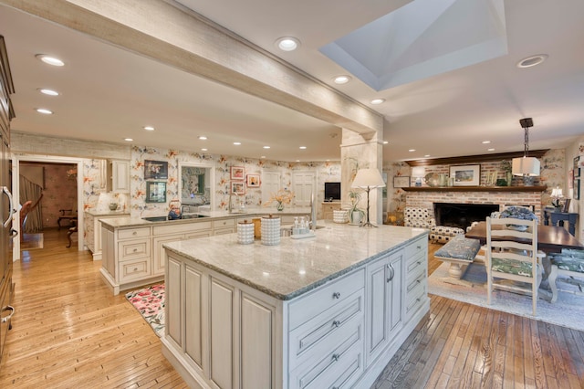 kitchen with light stone counters, light wood-type flooring, a large island, hanging light fixtures, and a brick fireplace