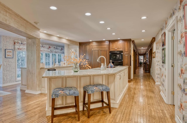 kitchen with oven, a large island, a kitchen bar, and light hardwood / wood-style flooring