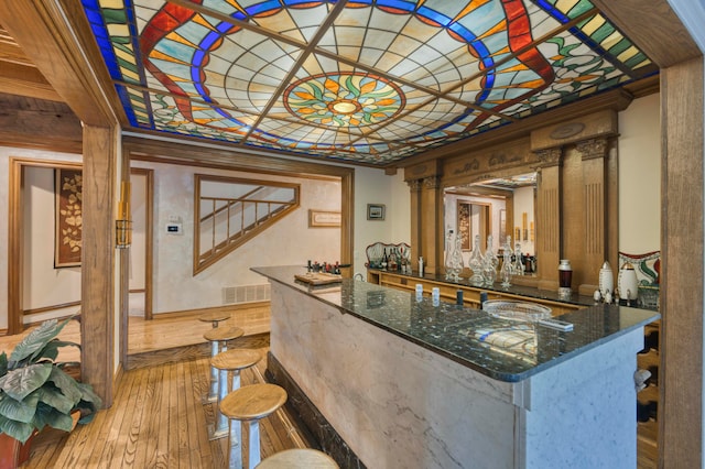 bar with dark stone counters, ornamental molding, and light hardwood / wood-style flooring