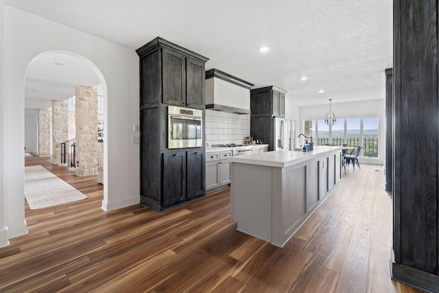 kitchen with tasteful backsplash, appliances with stainless steel finishes, a textured ceiling, a kitchen island with sink, and dark wood-type flooring